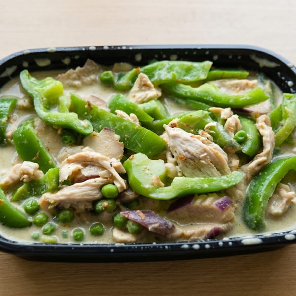 Green curry with chicken, bell peppers, and peas in a black takeout container.